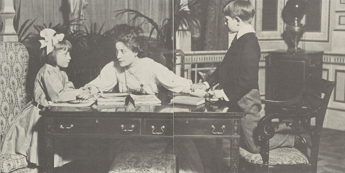 Eleanor Robson in The Girl Who Has Everything in 1906 is seen sitting at a desk with a young boy and girl holding her hands.