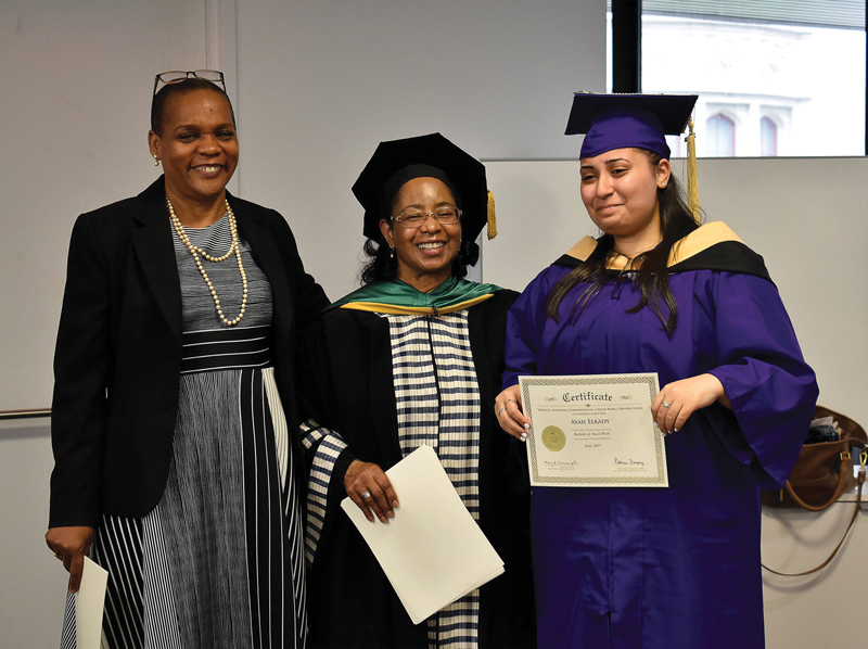 A new graduate poses with their certificate with the dean and another woman.