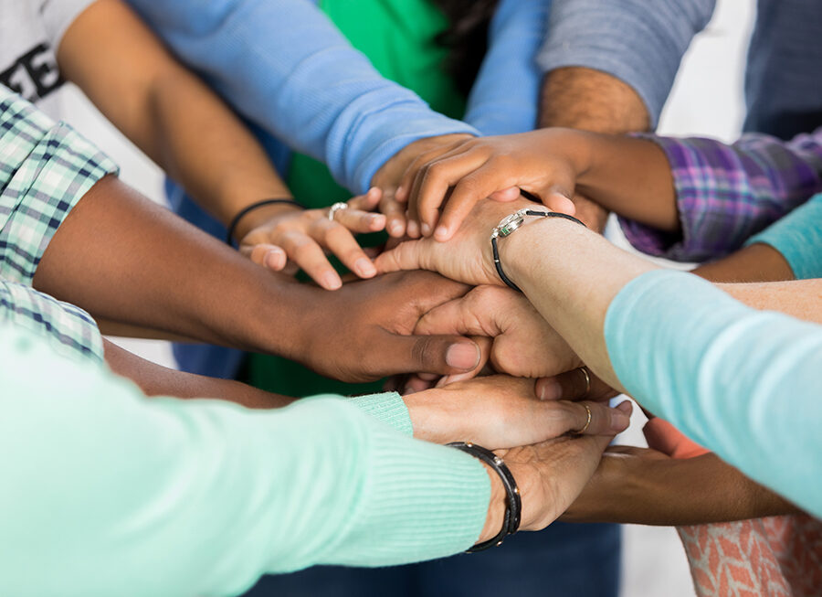 Diverse group of people put hands together in support. View is of hands and arms only.