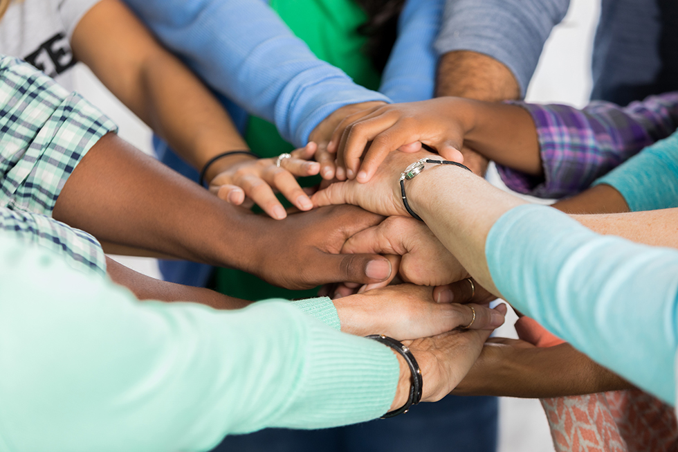 Diverse group of people put hands together in support. View is of hands and arms only.