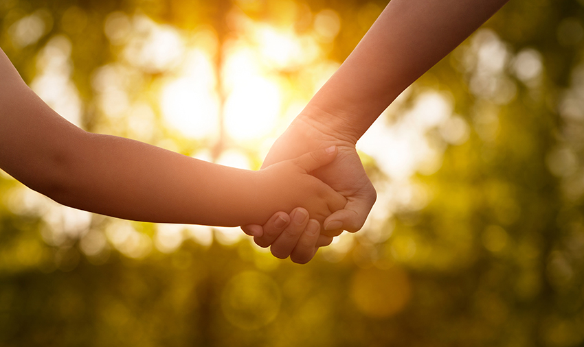 A mother and a child holding hands in the sunset.