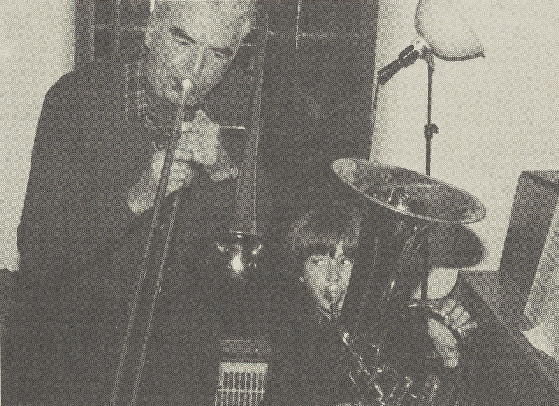 Making music with one of his grandsons in 1981. Lloyd MacMahon (left) is on the trombone and his grandson (right) on the tuba. A piano with sheet music is next to them.