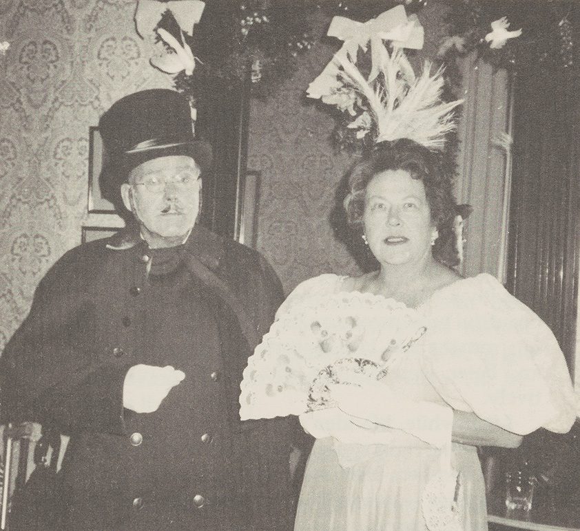 Jack and Audrey Madden dressed up at a fancy dress party in 1984. He is wearing a top hat and she is wearing a dress with a hat and a fan in her gloved hands.