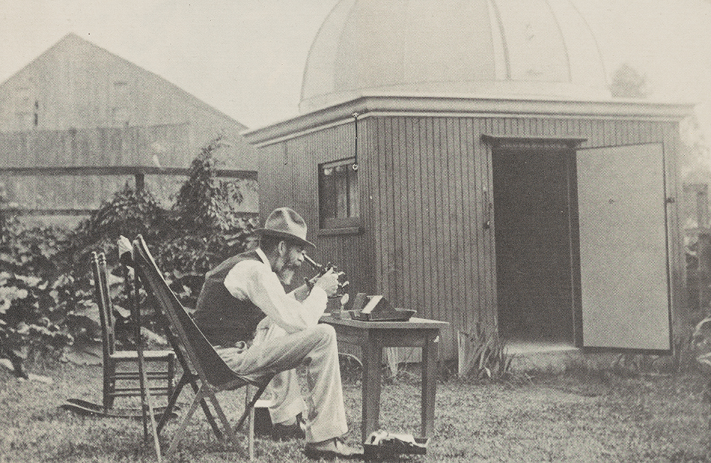 Yalden is sitting in a chair in a yard holding a device. His interest in astronomy led him to build an observatory in his own backyard.