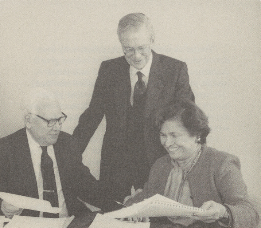 Herbert is standing in the middle of two other people sitting with papers in their hands. William Parsons, chairman of The Trust for 18 years, Herbert West, and Barbara Scott Preiskel, who became chairman in 1990.