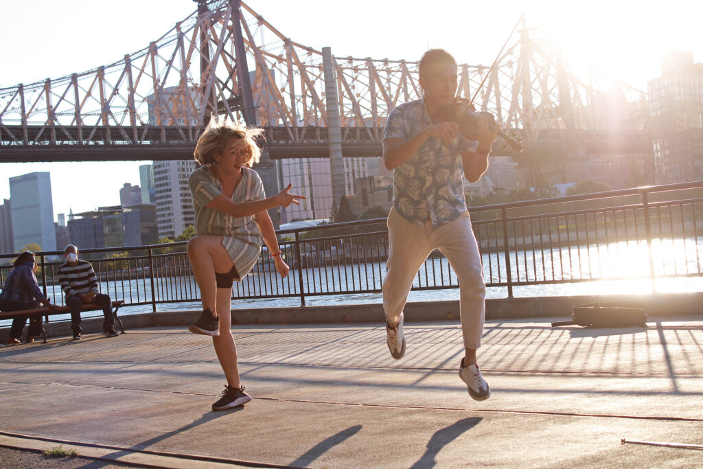 A dancer and a violinist perform in front of the Queensboro Bridge 