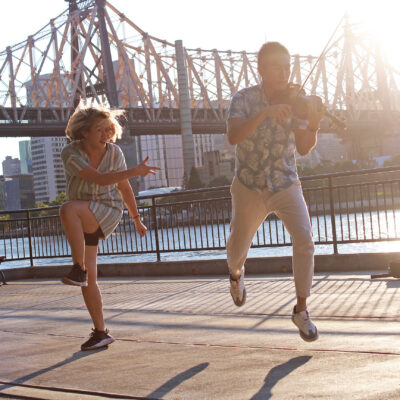 A dancer and a violinist perform in front of the Queensboro Bridge 