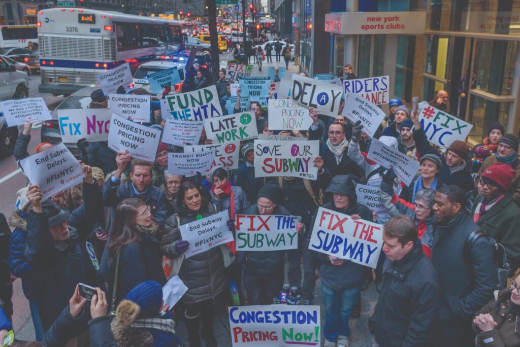 Protestors on a sidewalk holding signs calling for fixes to the New York City subway system.