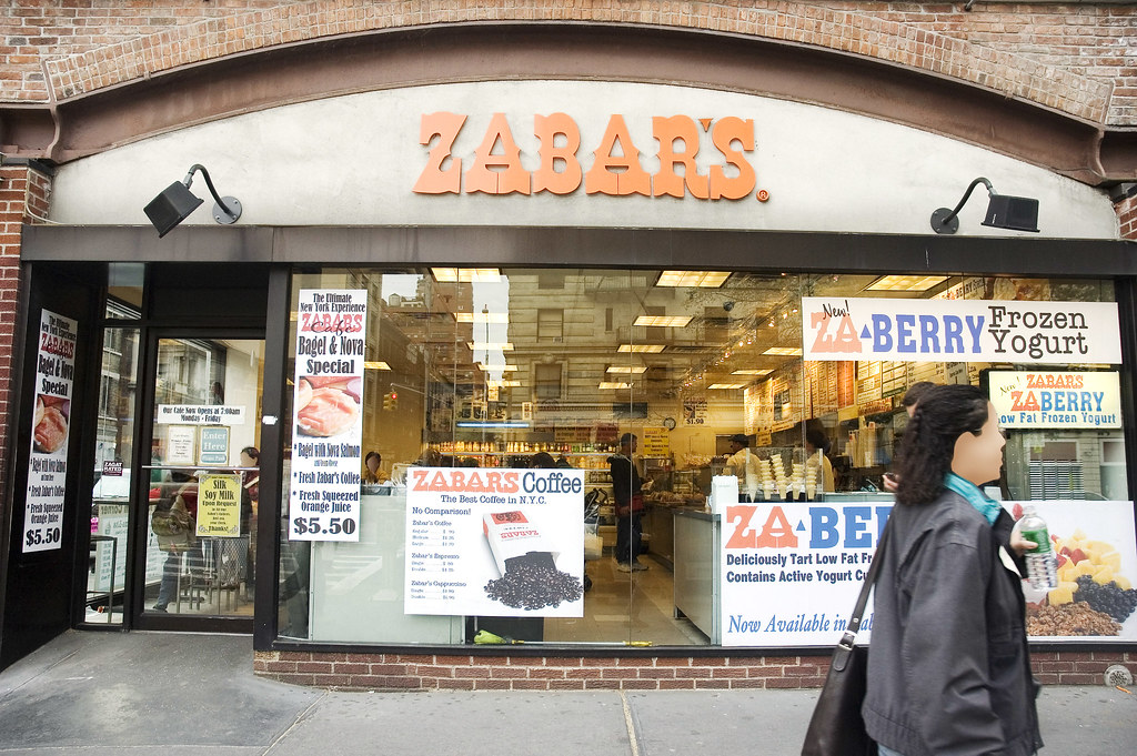 Woman walking past Zabar’s gourmet deli storefront.