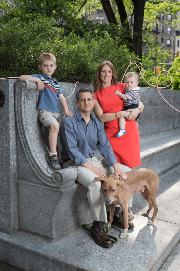 A young family and their dog sit on a bench.
