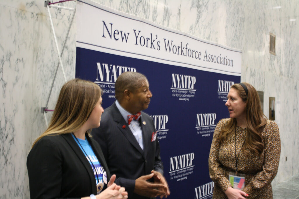 Three people speak at a meeting of New York’s Workforce Association. 