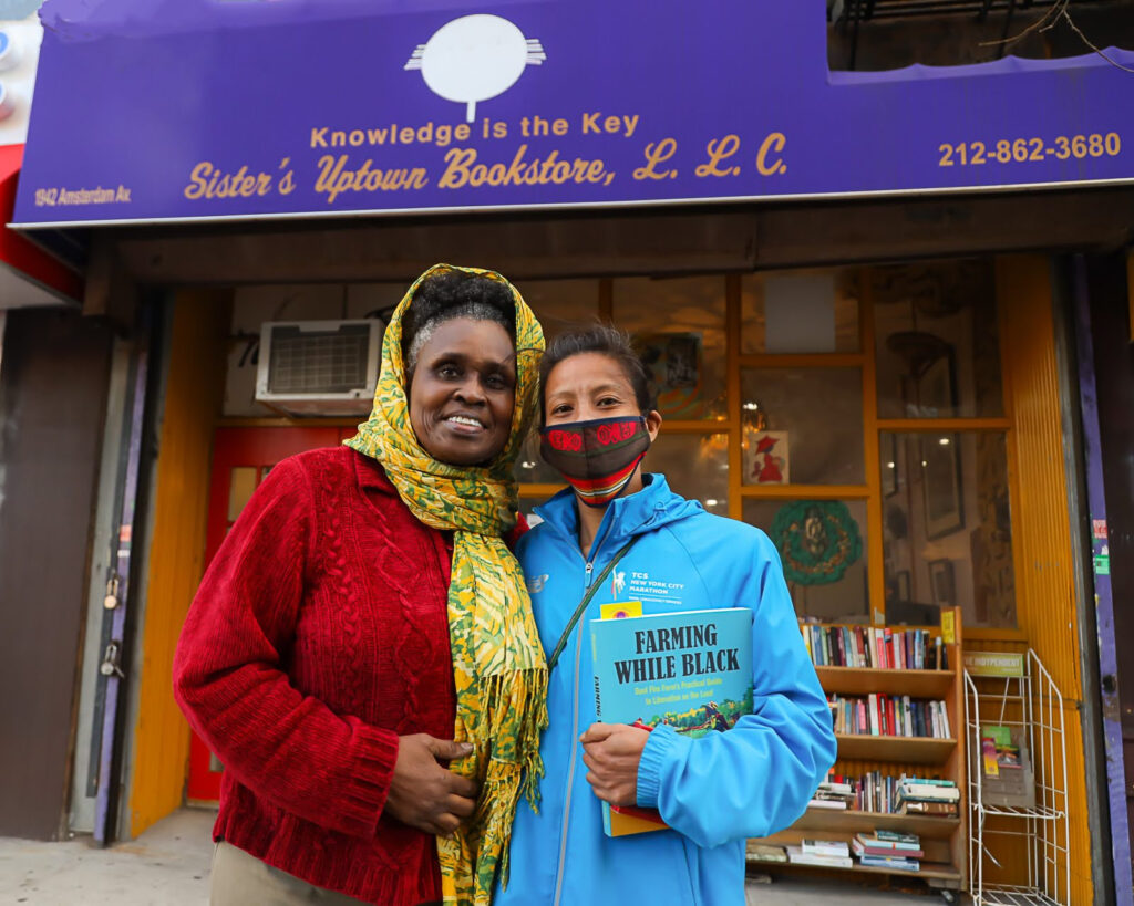 Two women pose for a picture in front of Sister's Uptown Bookstore