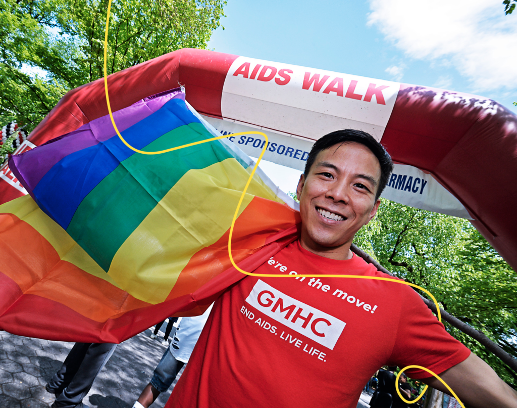 An Asian-American man in a GMHC tee-shirt holds a rainbow flag as he participates in an AIDS Walk in New York. 
