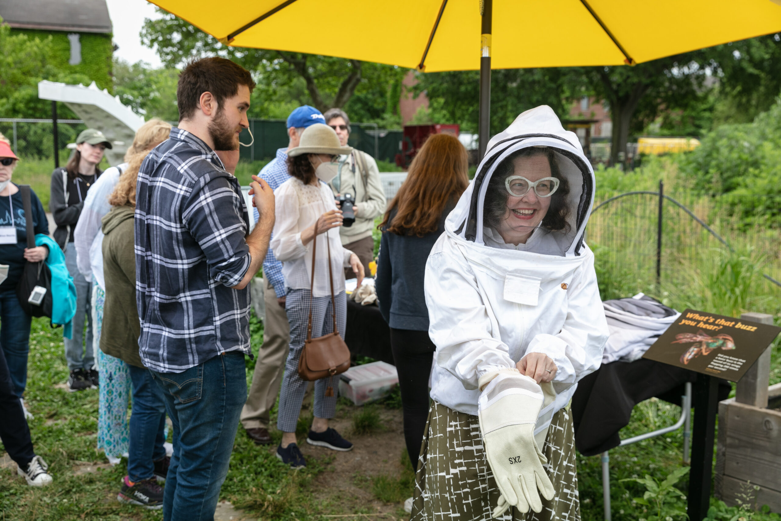 A small group of adults stands outdoors; a Trust donor puts on a bee suit so she can handle these live pollinators.