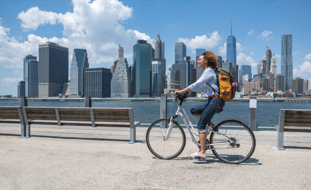 A woman biking with the NYC skyline behind her