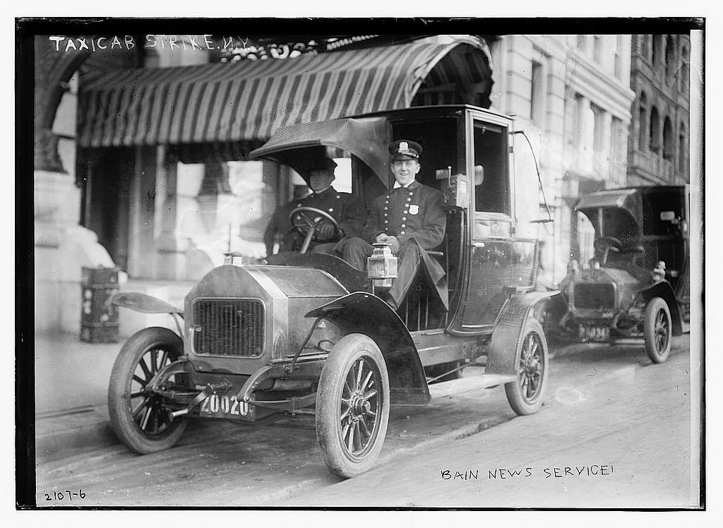 An electric taxicab in 1900 with a driver and passenger.