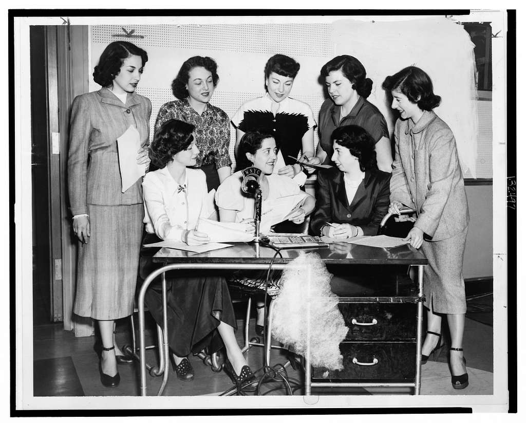 A group of women gather around a microphone labeled “WNYC.”