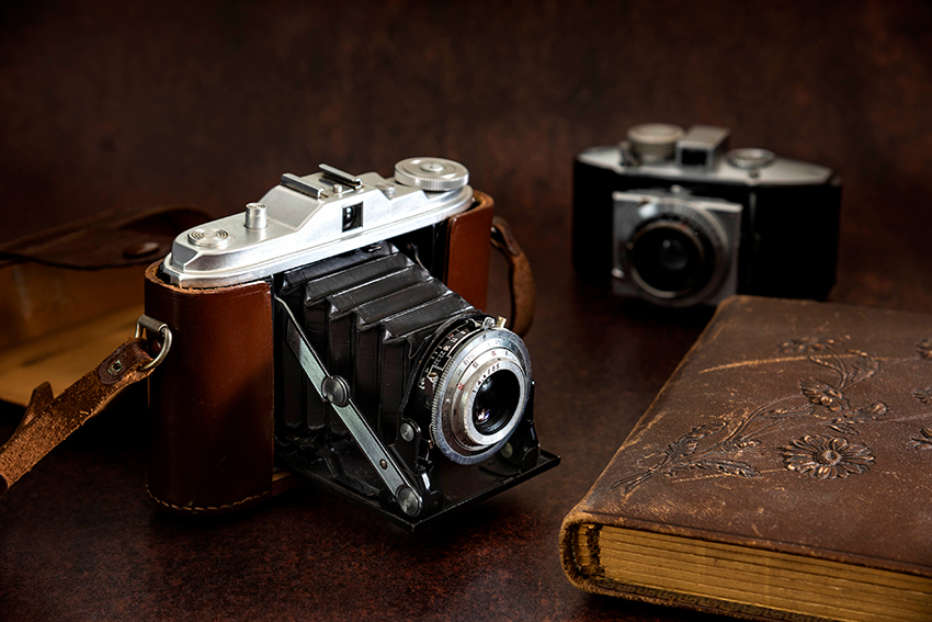 Antique folding bellows camera with leather strap and leather antique album. The bellow camera in the foreground is from the 1930s.