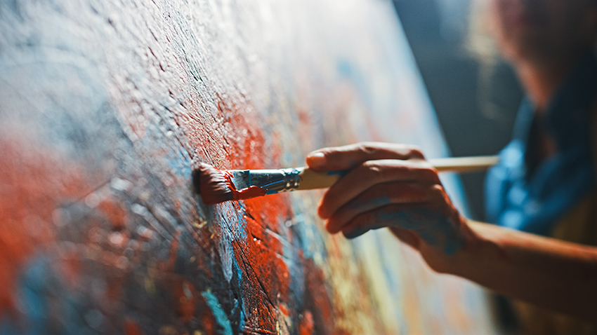 An artist puts their brush to the canvas filled with colorful paint strokes.