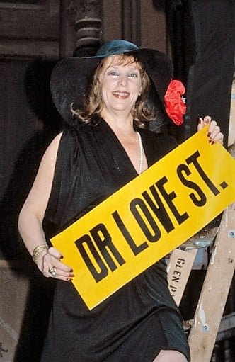 Gael Greene holding a sign that says “Dr Love St.”