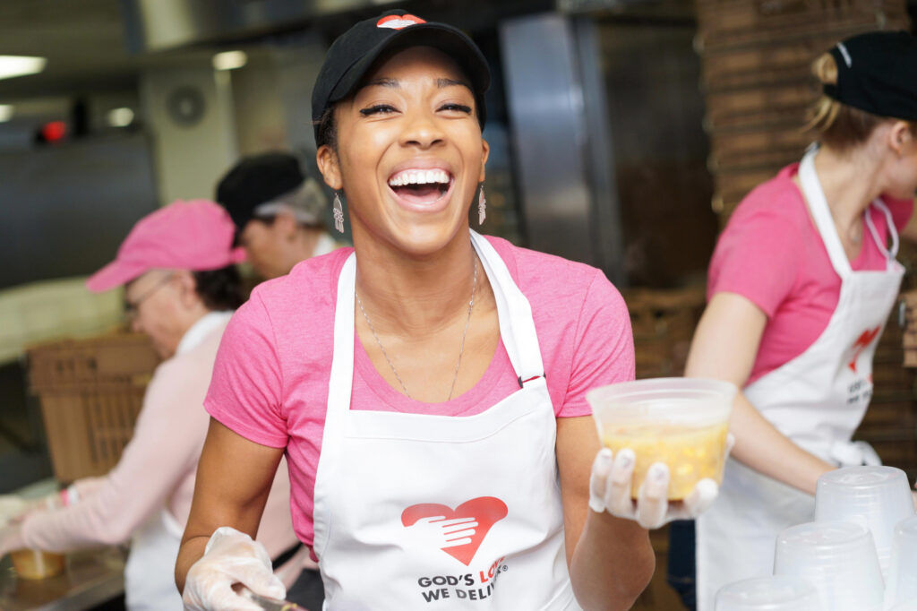 A God’s Love We Deliver volunteer smiling while serving soup.