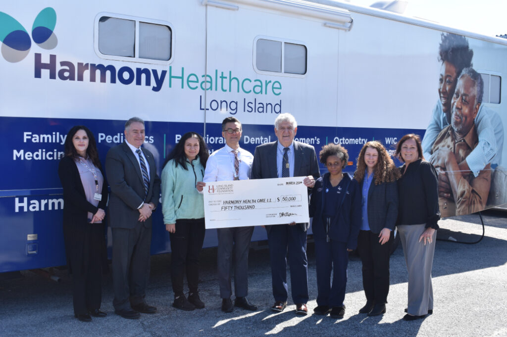 A group of people hold up an oversized check in front of a medical care trailer 