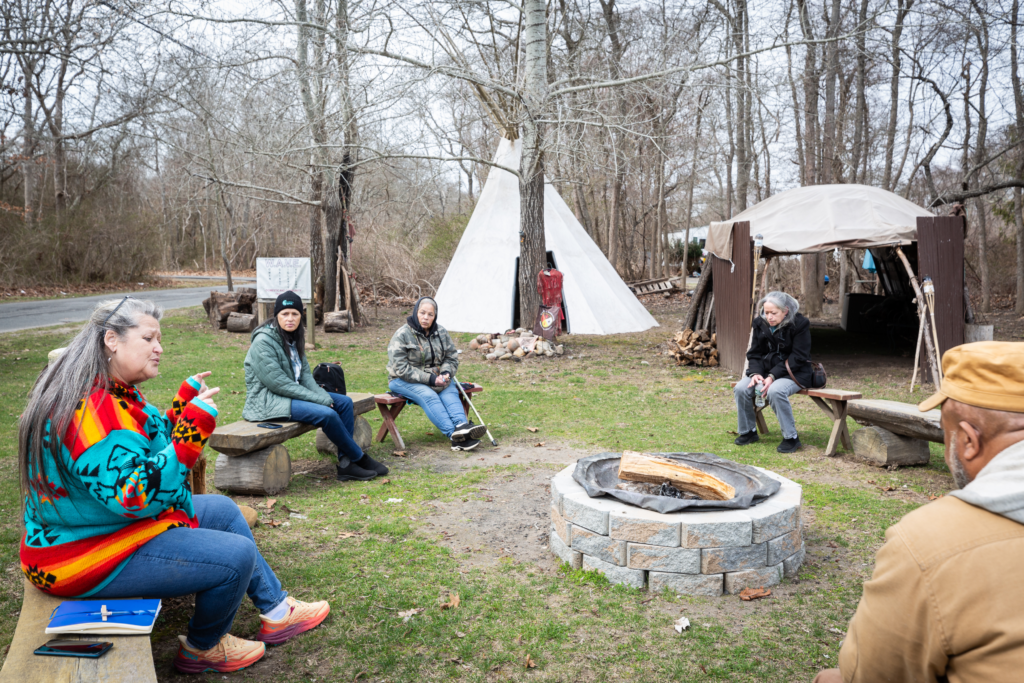 Adults sit around a fire pit in a prayer circle