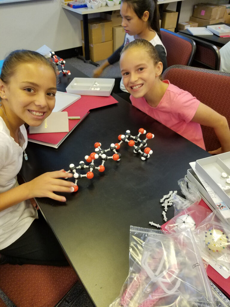 Two young girls smile in with a model of molecules