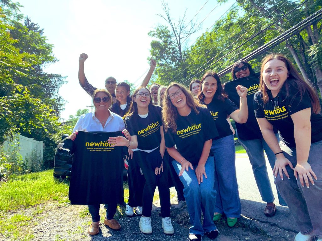 Photo of smiling adults holding black t-shirts with bright yellow text reading "New Hour"