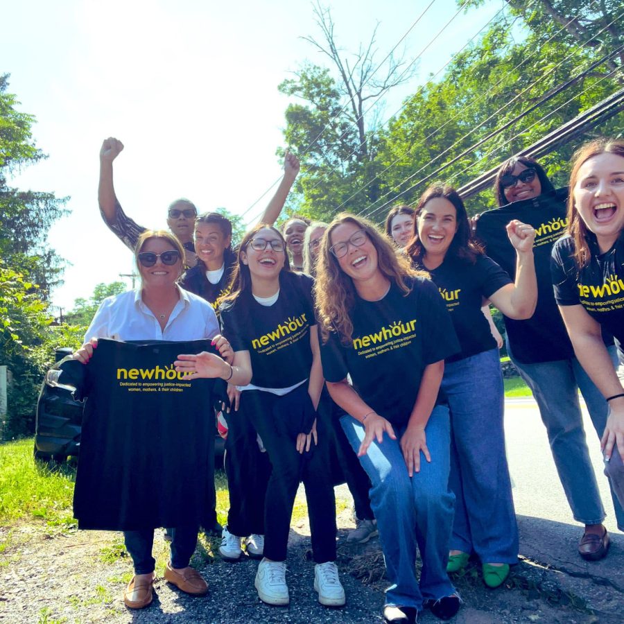 Photo of smiling adults holding black t-shirts with bright yellow text reading "New Hour"